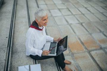 Business woman using laptop outdoors while sitting on the stairs.