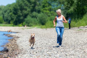mature woman jogs with a labrador retriever riverside