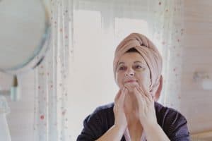 aged-elderly-beutiful-woman-in-bathrobe-and-towel-on-head-applies-cosmetics-cream-does-facial-massage_t20_QKke8k